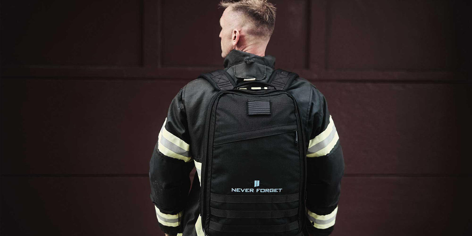 Man in firefighter jacket wearing black GORUCK backpack with Never Forget 9/11 patch against dark wall