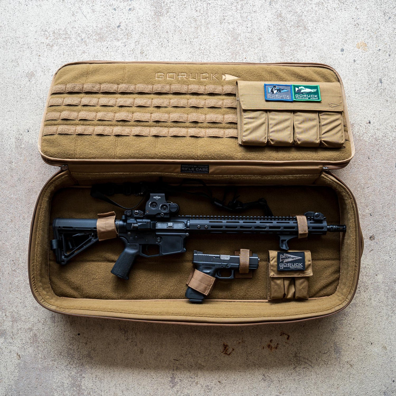 A black rifle and handgun in a tan GORUCK gun case with pouches, placed on a concrete floor.