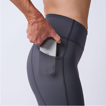 Person placing a smartphone into the side pocket of black athletic leggings.