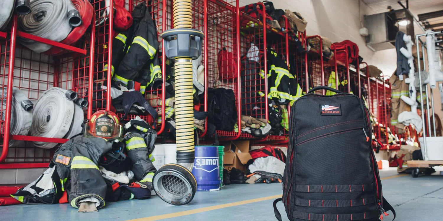 GORUCK black rucksack in fire station gear room with firefighter helmets, jackets, and hoses