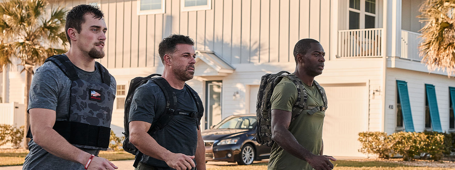 Three men wearing weighted vests walk outside in a residential neighborhood on a sunny day.