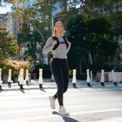 Woman rucking with GORUCK backpack, crossing city street in athletic gear, outdoor fitness