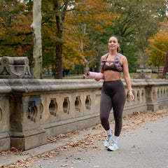 Woman rucking in GORUCK weighted vest, activewear, and holding a yoga mat outdoors in fall