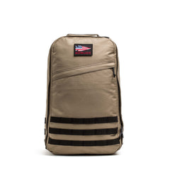 The GR1 USA - Cordura is a tan tactical backpack with a front zipper pocket, black horizontal straps, and a US flag patch—an everyday carry rucksack inspired by Special Forces grade gear like the GORUCK GR1.