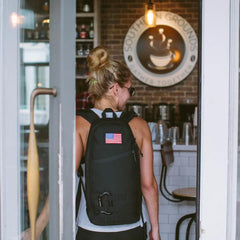 Woman wearing GORUCK black rucksack with American flag patch entering a coffee shop