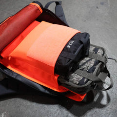 Open backpack on ground with neatly packed orange and black bags, pouches, and the Sand Ruck Plate Bundle inside.