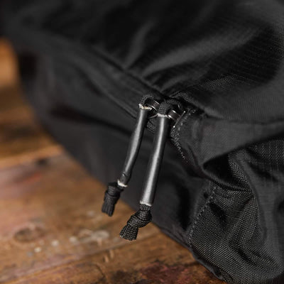 Close-up of a water-resistant GORUCK Shoe Bag made from black Ripstop ROBIC® fabric, featuring two zippers with black pull cords. This functional bag elegantly rests on a wooden surface, showcasing the grain and texture.