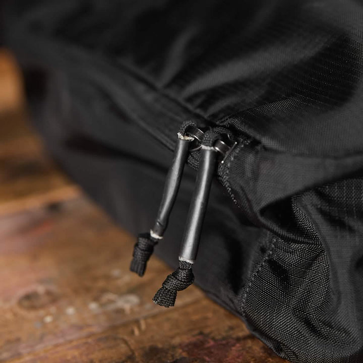 Close-up of a water-resistant GORUCK Shoe Bag made from black Ripstop ROBIC® fabric, featuring two zippers with black pull cords. This functional bag elegantly rests on a wooden surface, showcasing the grain and texture.
