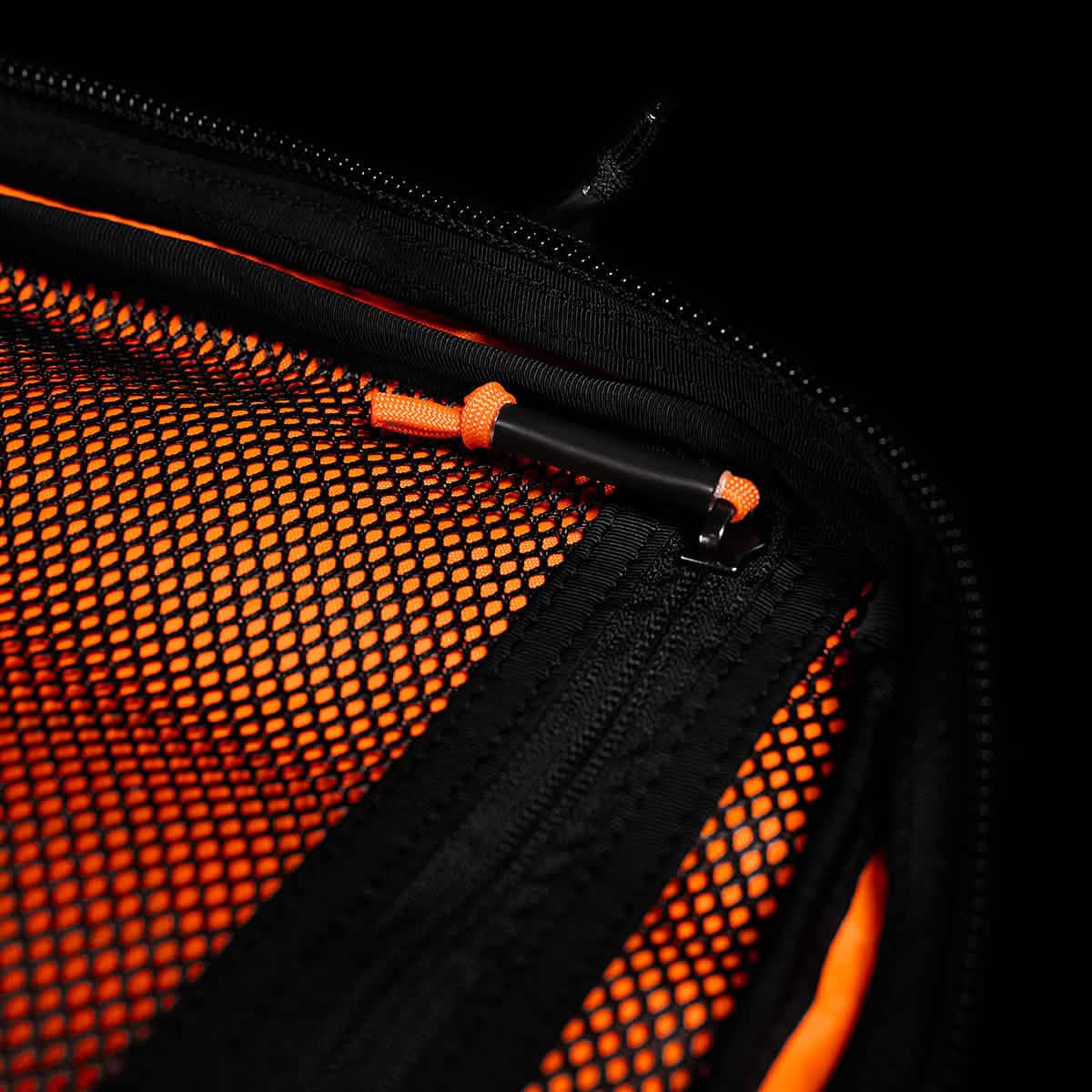 Close-up of a GR2 USA x Carryology - Ultra Black mesh zipper pocket made from Challenge Sailcloth UHMWPE, with an orange pen clipped inside, set against an orange background.
