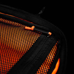 Close-up of a GR2 USA x Carryology - Ultra Black mesh zipper pocket made from Challenge Sailcloth UHMWPE, with an orange pen clipped inside, set against an orange background.