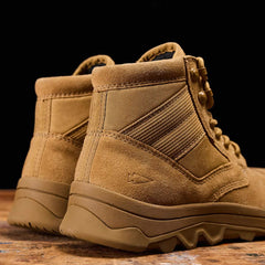 A close-up of GORUCK's MACV-2 Safety Boot - Mid Top, crafted from tan-colored suede, is displayed on a wooden surface highlighting its rugged soles and visible stitching designed to meet Special Forces Standards. These work boots provide an eye-catching contrast against the dark background while ensuring both durability and style.