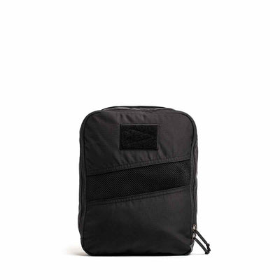 The GORUCK Shoe Bag - Ripstop ROBIC® is a compact black backpack with a straightforward, water-resistant design. It includes a front mesh pocket and features a top zipper for easy access. Its rectangular shape is enhanced by a discreet patch at the top center, offering versatility for any occasion against its simple white background.