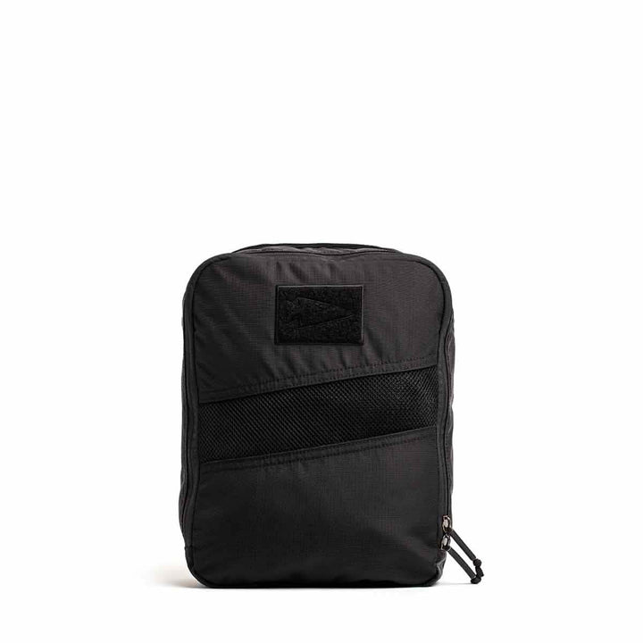 The GORUCK Shoe Bag - Ripstop ROBIC® is a compact black backpack with a straightforward, water-resistant design. It includes a front mesh pocket and features a top zipper for easy access. Its rectangular shape is enhanced by a discreet patch at the top center, offering versatility for any occasion against its simple white background.
