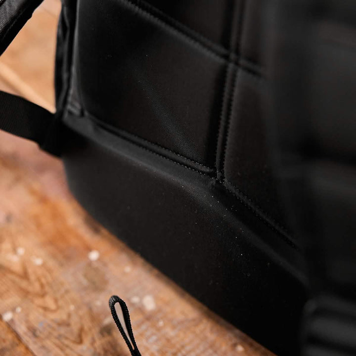 Close-up of a GORUCK KR1 kids rucksack on a wooden surface. The image highlights the backpack's padded straps and sturdy construction. A loop is visible at the bottom, attached to the bag, making it perfect for school supplies.