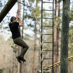 Man climbing thick rope on outdoor obstacle course in rugged GORUCK gear, forest background