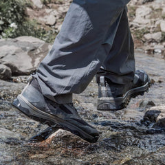 Close-up of durable waterproof hiking shoes stepping on wet rocky terrain with outdoor pants