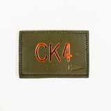 The Patch - Custom Leather Monogram is a green rectangular leather patch featuring "CK4" embroidered in orange with a small arrow embossed on the right—ideal for displaying your custom initials.