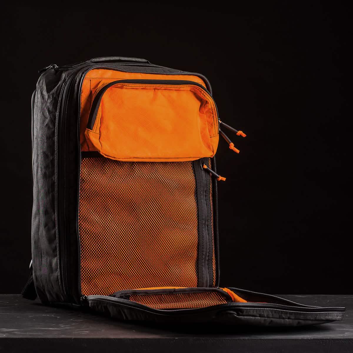 A GR2 USA x Carryology - Ultra Black backpack, made from durable UHMWPE fabric with orange mesh compartments open, is displayed against a black background.