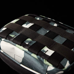 A close-up of the GORUCK GR1 Field Pocket x Gear Patrol, showcasing its black strap grid set against a black background. Its intricate Variegated Elephant Ear Camo design enhances the rugged style of this versatile accessory.