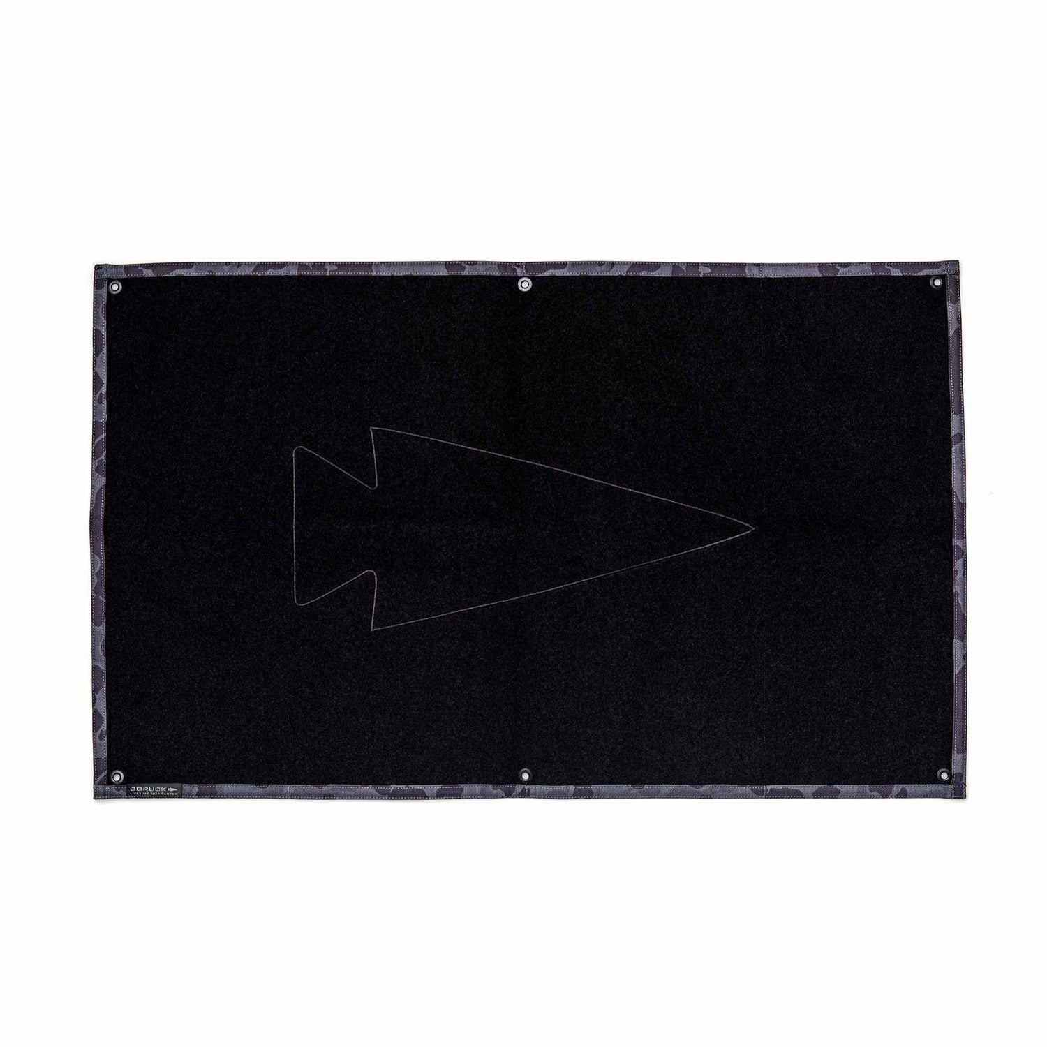 The GORUCK Patch Board is a rectangular black display featuring a subtle outlined arrowhead in the center and metal-reinforced holes along the edges, ideal for showcasing your favorite velcro patches.