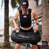 A man wearing the Training Weight Vest - Black lifts a heavy duffel bag outside near a brick building and palm tree.
