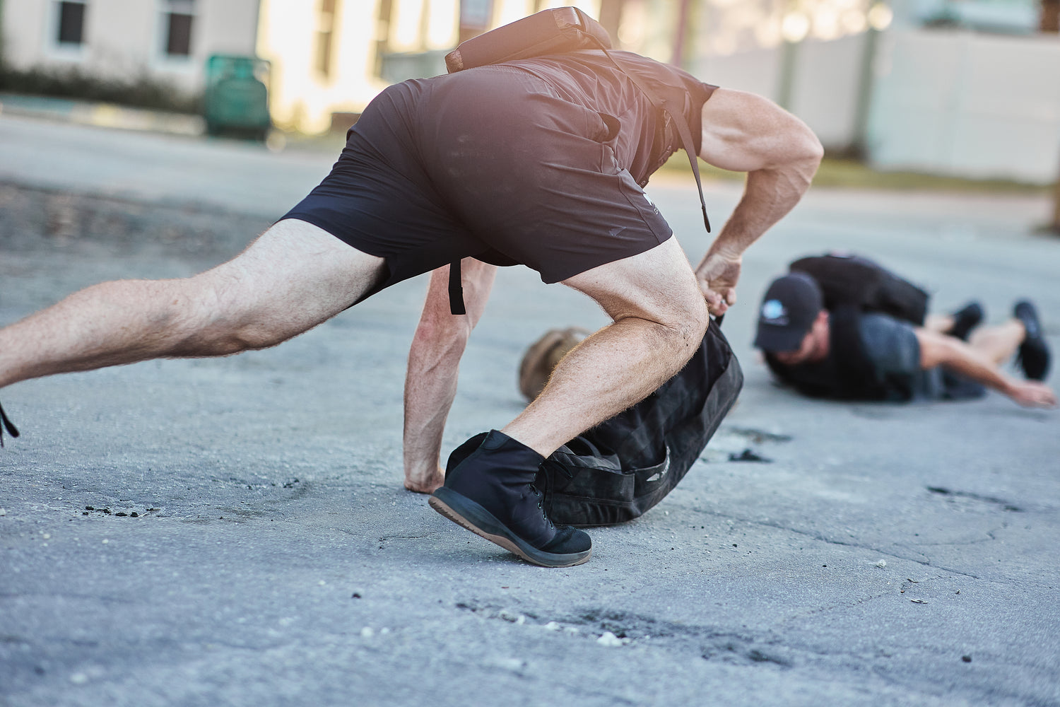Two people on the ground, one reaching for an RPC Long + 30LB (Long) Plate Bundle with the plate visible on the pavement in an outdoor urban setting.