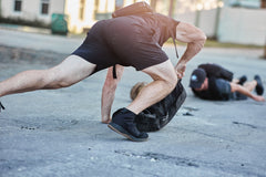 Two people on the ground, one reaching for an RPC Long + 30LB (Long) Plate Bundle with the plate visible on the pavement in an outdoor urban setting.