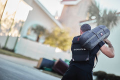 Man carrying a RPC Long + 30LB (Long) Plate Bundle on his shoulder, wearing a backpack with ergonomic lumbar support, walking outdoors.