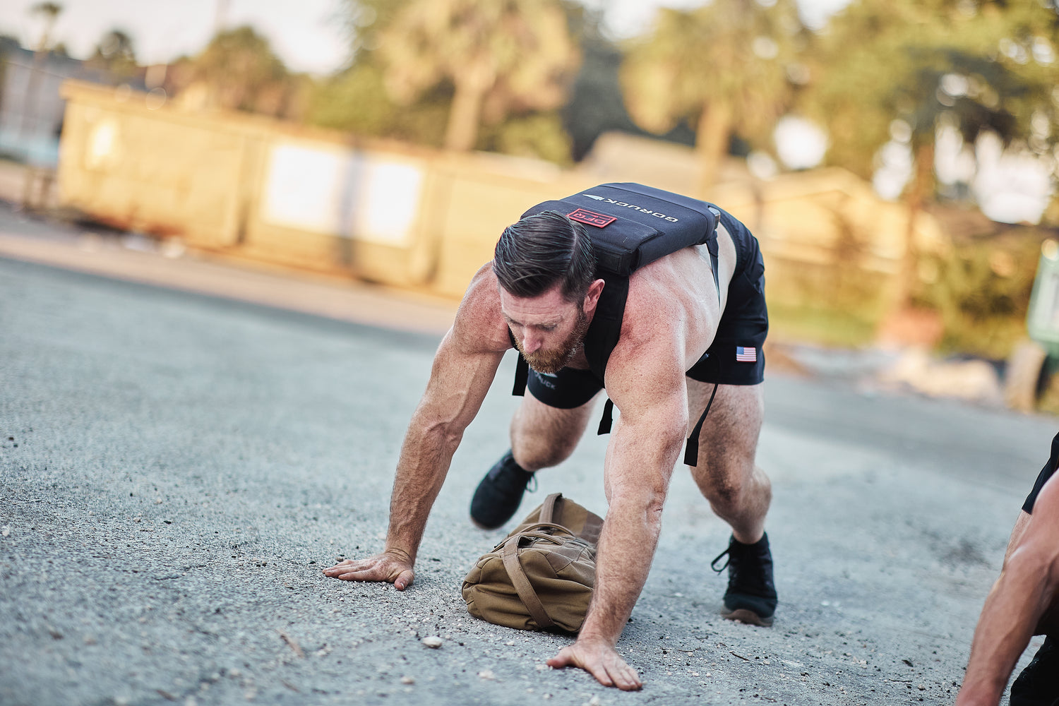 A man in workout gear does a bear crawl outdoors, facing the ground and wearing the RPC Long + 30LB (Long) Plate Bundle, which features ergonomic lumbar support.