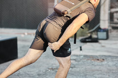 Man in athletic gear bends forward outdoors, holding his leg, wearing the RPC Long + 30LB (Long) Plate Bundle backpack for weighted training on a sunny day.
