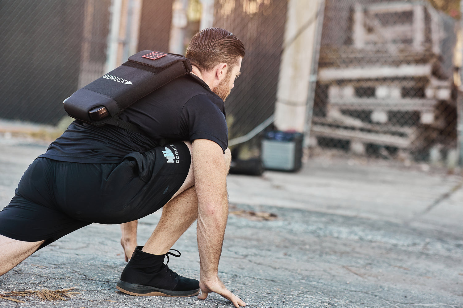 Man stretching outdoors on pavement, wearing black athletic clothes and the RPC Long + 30LB (Long) Plate Bundle weight vest with ergonomic lumbar support.