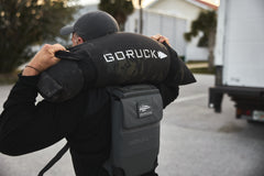 A person carries the RPC 3.0 backpack with a 10lb Ruck Sandplate on their shoulders outdoors for weighted training.