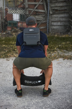 Man squatting outdoors with the RPC 3.0 + 10lb Ruck Sandplate, preparing for weighted training.