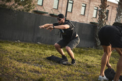 Man wearing the RPC 3.0 and sunglasses does squats outdoors, with a 10lb Ruck Sandplate on the ground in front of him and a cap on his head.