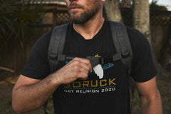A man in a black "GORUCK GRT Reunion 2020" shirt adjusts his gray backpack outside, getting ready for weighted training with the RPC 3.0 + 10lb Ruck Sandplate.