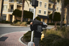 A person carries an RPC 3.0 + 10lb Ruck Sandplate and walks near an apartment building on a city street corner.