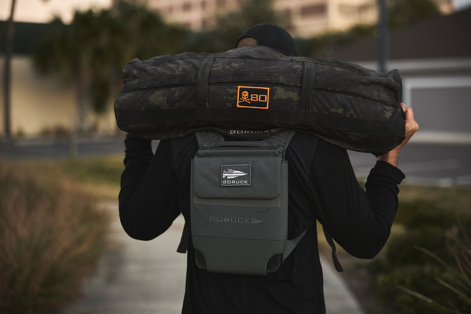 Outdoors, a person shoulders a 10lb Ruck Sandplate while wearing the RPC 3.0 for added weight training.