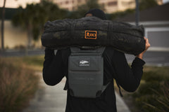 Outdoors, a person shoulders a 10lb Ruck Sandplate while wearing the RPC 3.0 for added weight training.