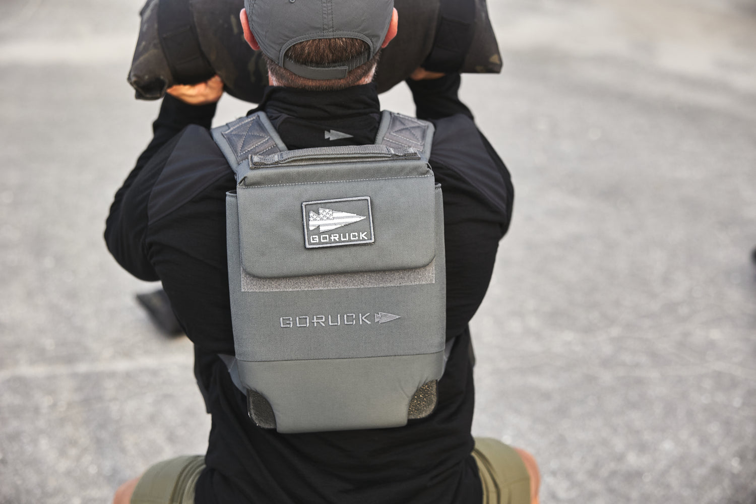 A person wears the RPC 3.0 with a 10lb Ruck Sandplate and lifts a heavy object outdoors on pavement, ideal for weighted training.