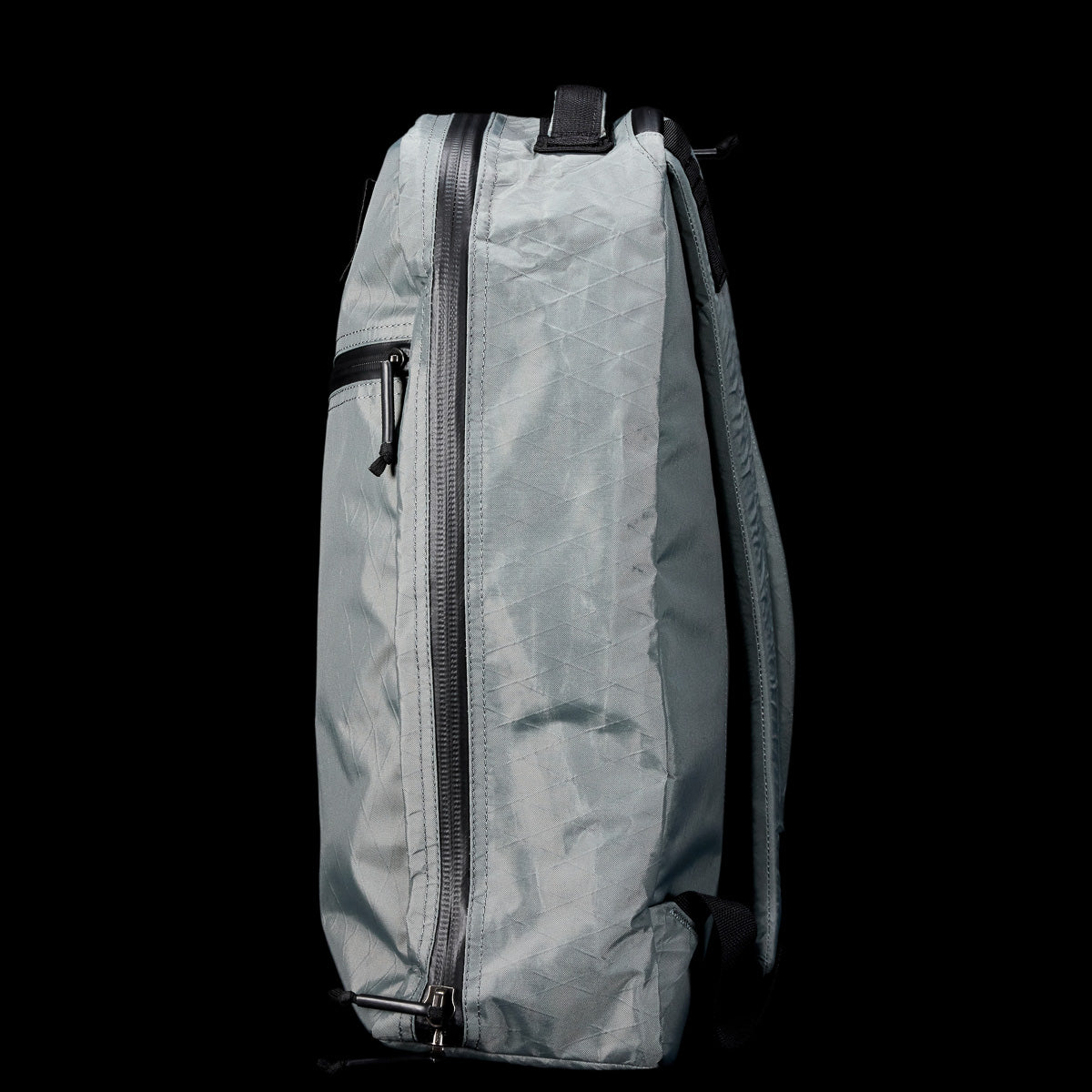 Side view of the Bullet X-PAC, a light gray weatherproof daypack with a black zipper, made from durable X-PAC material, set against a solid black background.
