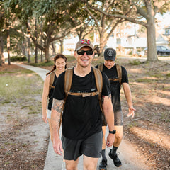 Three people walk and smile on a sunny, tree-lined path, each wearing backpacks equipped with the Training Sternum Strap for adjustable weight distribution.