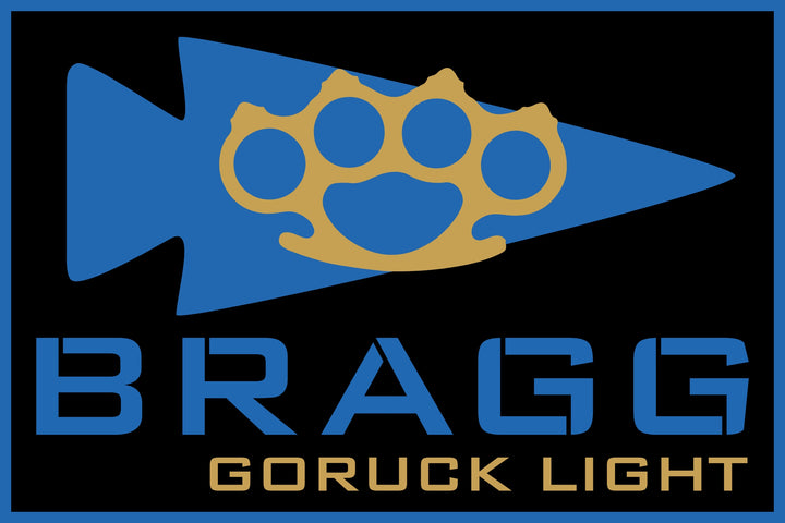 Blue arrowhead with a gold brass knuckle inspired by Special Forces training. "BRAGG EVENT WEEKEND 2026" appears below the design.