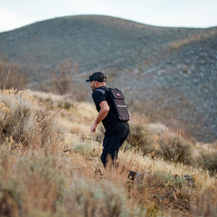 A man wearing the Ruck Plate Carrier 3.0 with ergonomic lumbar support runs up a dry, grassy hillside with mountains in the background.