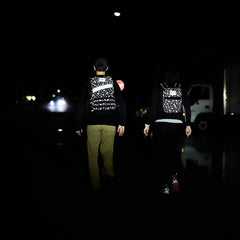 Two people with Rucker 4.0 - Reflective Spearhead rucksacks walk at night on a dark street, distant lights shining ahead.