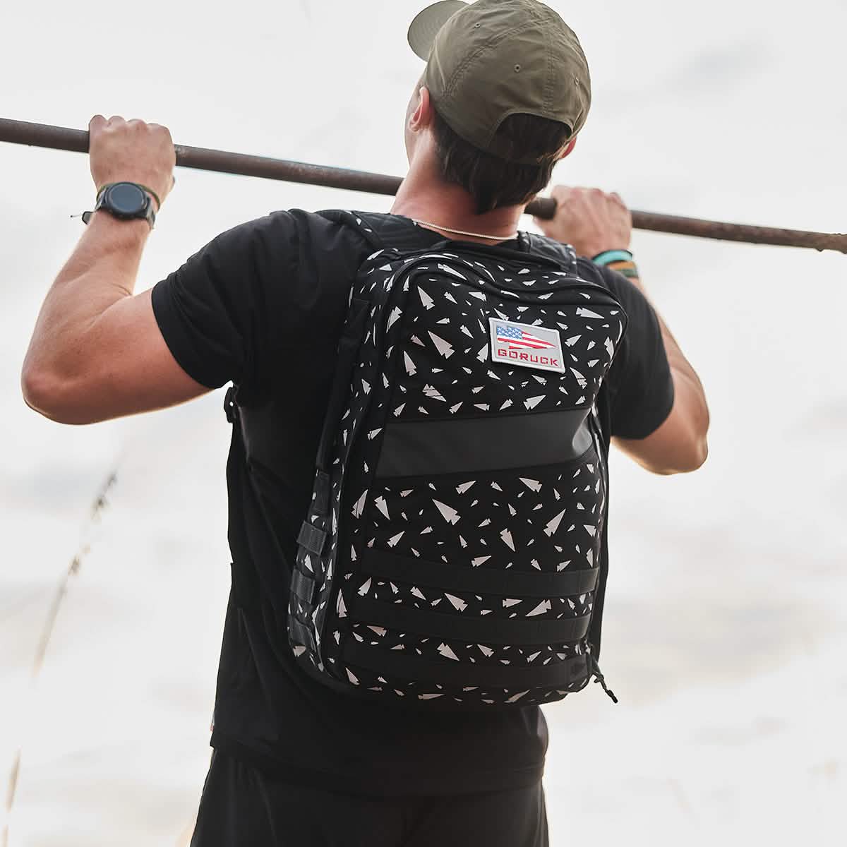 Wearing the Rucker 4.0 - Reflective Spearhead backpack, a man grips a bar and prepares for an intense rucking workout.