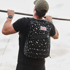 Wearing the Rucker 4.0 - Reflective Spearhead backpack, a man grips a bar and prepares for an intense rucking workout.