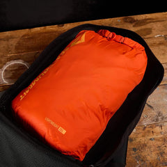 Orange lightweight 20L dry bag packed inside a black rucksack on wooden surface