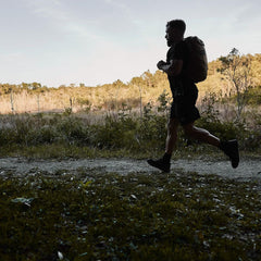 Man running on a trail wearing black gear and a rucksack in a natural outdoor setting