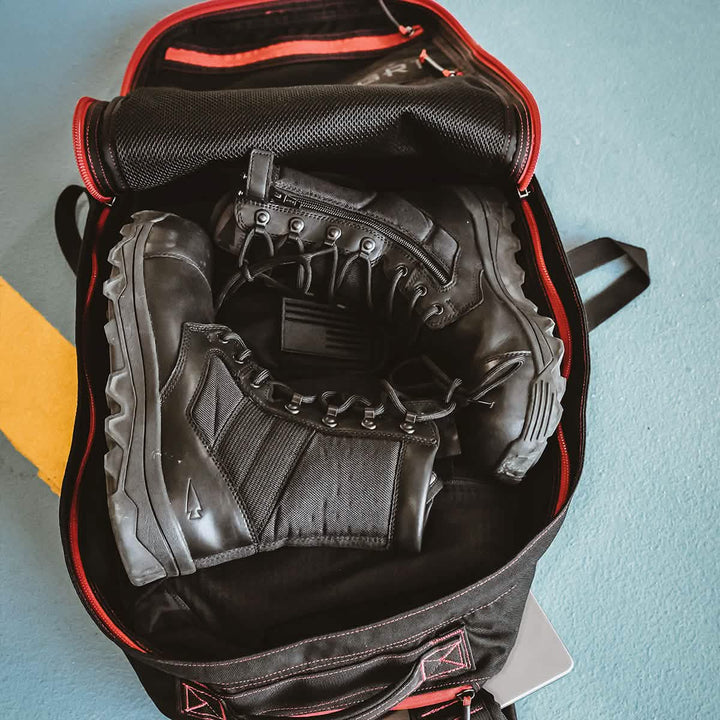 A pair of MACV-2 Safety Boots - High Top by GORUCK, designed to Special Forces standards, is neatly packed inside an open black and red duffel bag, resting on a blue and yellow floor.
