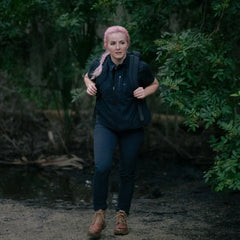 Woman with pink braided hair hiking through forest wearing black activewear and a GORUCK backpack